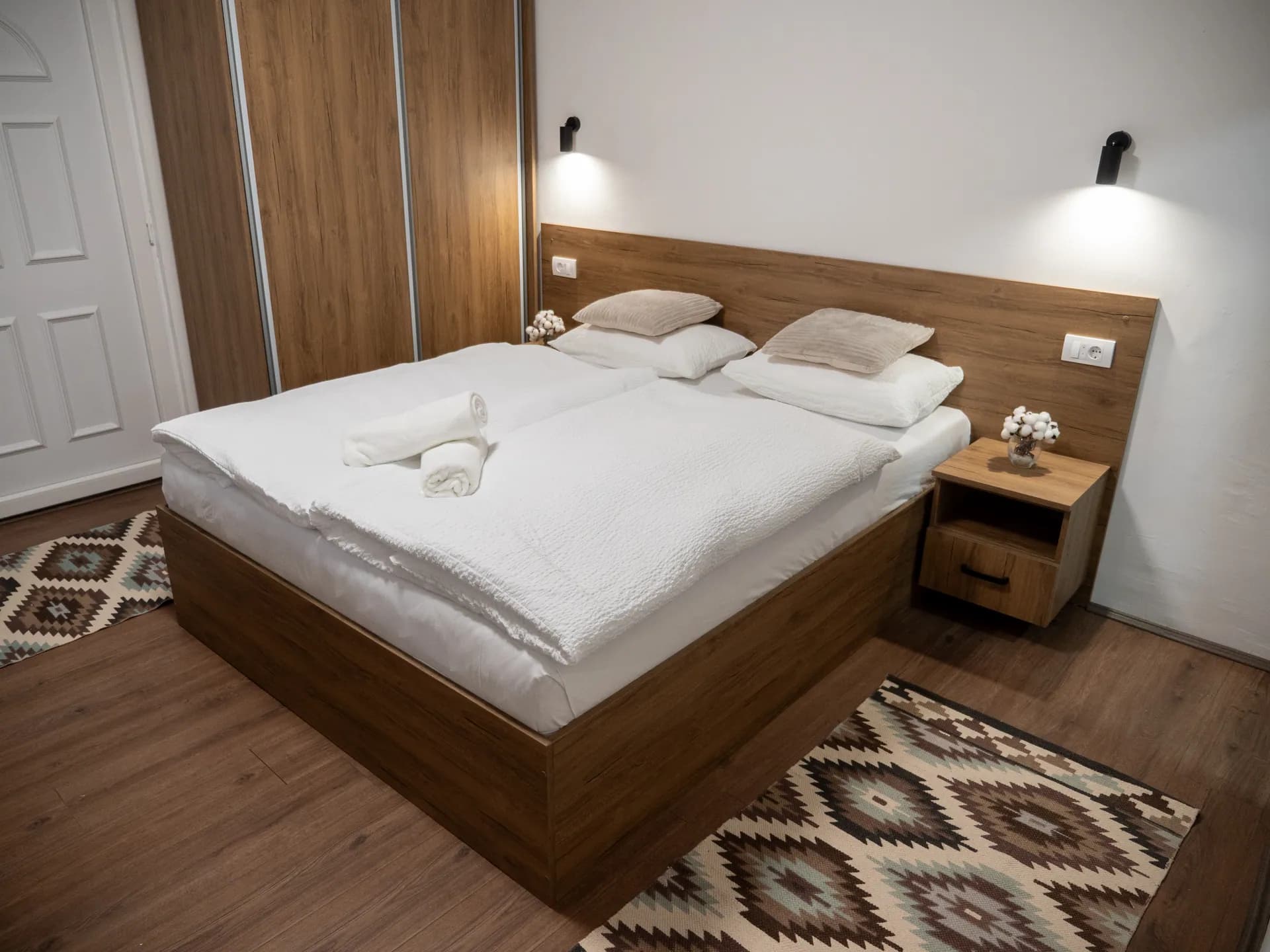 Apartman I — bračni krevet sa drvenim uzglavljem, noćnim ormarićem i tkanim tepihom