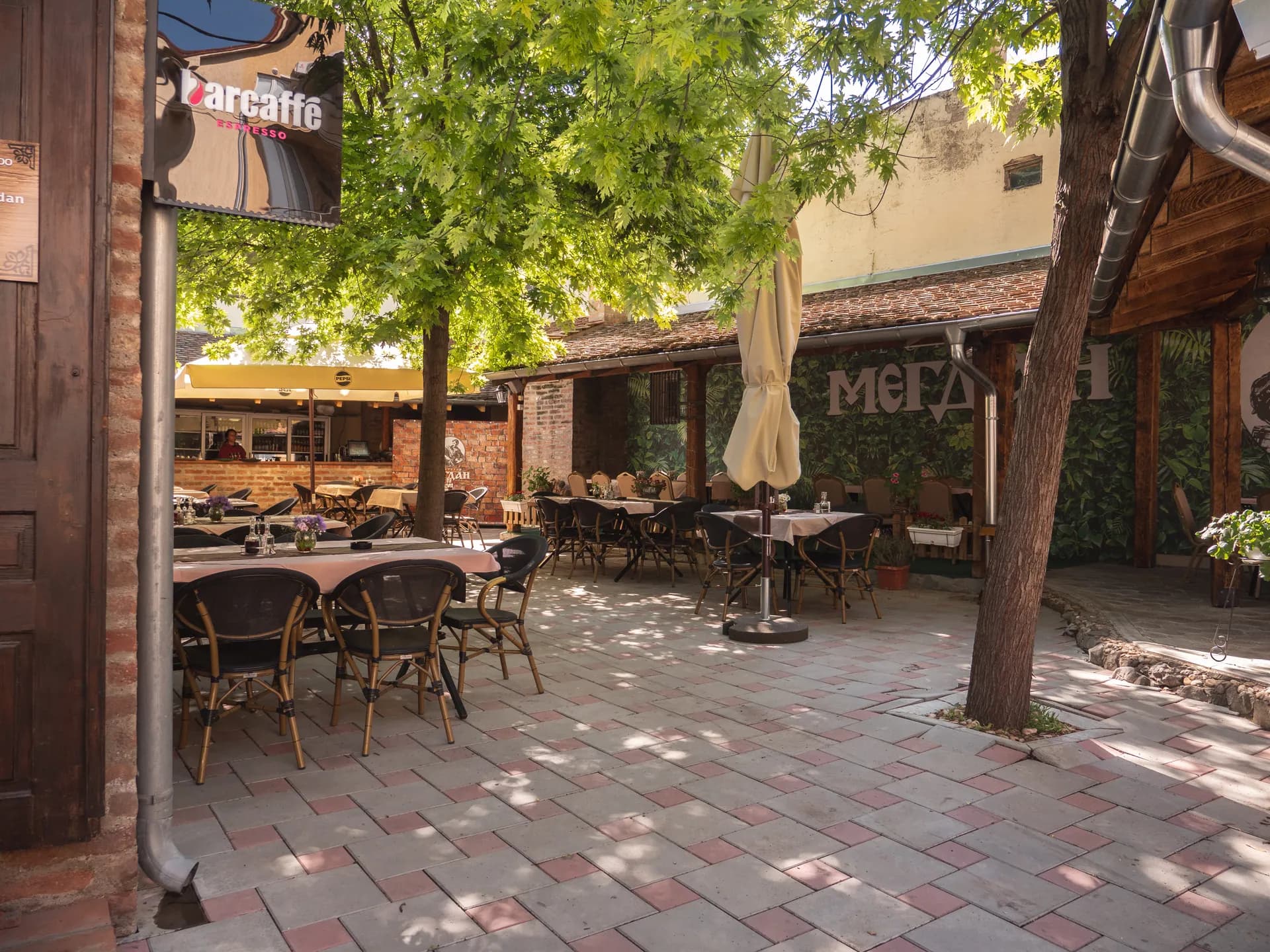 Bašta sa drvetom u sredini i stolovima uz ciglane zidove