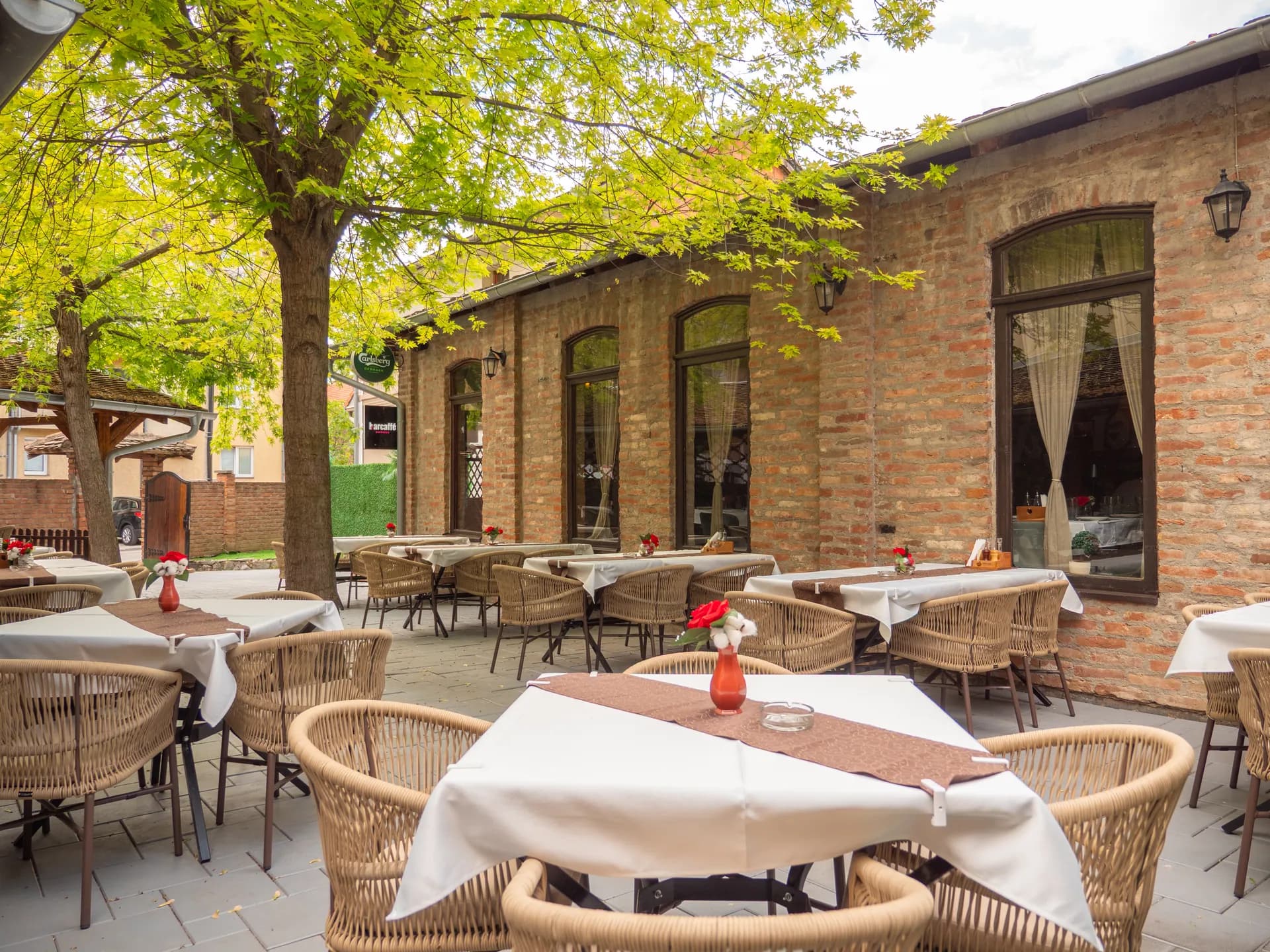Letnja bašta sa belim stolnjacima uz ciglanu zgradu restorana